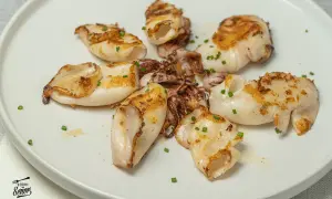 Deliciosos chipirones a la plancha, dorados y tiernos, servidos en un plato blanco con cebollino picado.