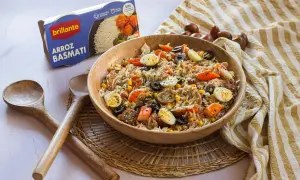 Delicioso arroz con atún, huevo duro, aceitunas y maíz en un bol de madera. Acompañado de cucharas de madera y una caja de arroz basmati.