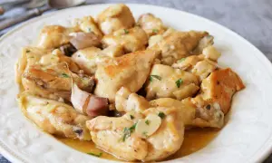 Sabroso pollo al ajillo servido en un plato blanco, con trozos de pollo dorados y dientes de ajo enteros.