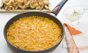 Arroz con sepia en paellera, acompañado de patatas fritas y una salsa cremosa.