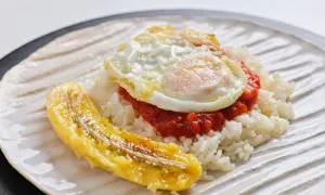 Un plato de arroz a la cubana con huevo frito, salsa roja y plátano maduro frito.