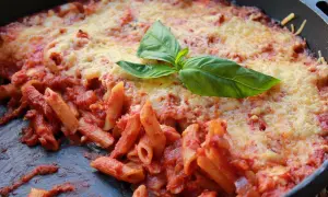 Macarrones al horno con salsa de tomate y queso gratinado, decorados con hojas de albahaca fresca. ¡Un plato casero irresistible!