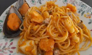 Espaguetis a la marinera con mejillones, gambas y calamares, servidos en un plato con un delicado estampado floral.