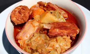 Un reconfortante plato de patatas con costillas, repollo y chorizo en un cuenco rosa.