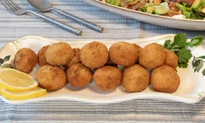Croquetas de pollo doradas y crujientes en una bandeja decorada, acompañadas de rodajas de limón y perejil.