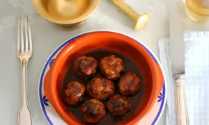 Un cuenco de barro con deliciosas albóndigas en salsa, listo para ser disfrutado con tenedor y cuchillo.