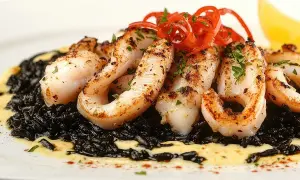Delicioso arroz negro con calamares a la plancha, adornado con pimientos rojos y perejil.