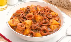 Un tazón de patatas con calamares en salsa, acompañado de pan rústico y una pizca de pimentón.