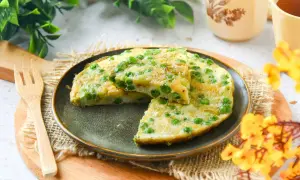 Tortilla de guisantes recién hecha, con trozos de patata y guisantes verdes, servida en un plato oscuro.