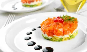 Delicioso tartar de salmón con aguacate, coronado con granada y eneldo. Un plato elegante con un toque de salsa balsámica.