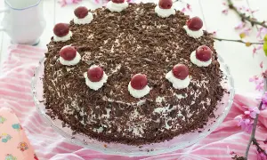 Deliciosa tarta Selva Negra, cubierta de virutas de chocolate y coronada con cerezas y nata. Perfecta para cualquier celebración.