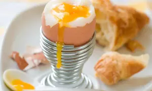 Un huevo pasado por agua con su yema dorada cayendo, listo para ser disfrutado con un croissant.