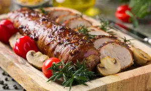 Lomo de cerdo al horno jugoso, glaseado y especiado, servido con champiñones, pimientos rojos y romero en tabla de madera.