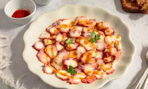 Delicioso carpaccio de pulpo con pimentón y perejil, servido en plato blanco. Acompañado de pan tostado y especias.