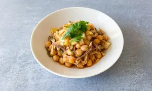 Un plato de ropa vieja canaria, con garbanzos, carne deshebrada y patatas fritas, adornado con perejil fresco.