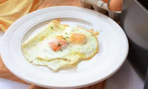 Dos huevos fritos perfectos, cocinados en freidora de aire, servidos en un plato blanco. Un toque de cebollino fresco adorna las yemas.