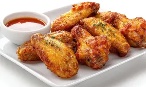 Alitas de pollo al horno crujientes, doradas y sazonadas con hierbas, servidas con una salsa picante.