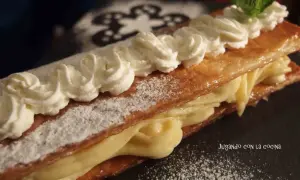 Delicioso milhojas de crema, con hojaldre crujiente y relleno cremoso, decorado con nata montada y una hoja de menta.