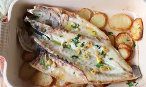 Lubina a la espalda horneada con patatas, ajo y perejil en una bandeja.