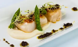 Deliciosas vieiras a la plancha sobre puré cremoso, adornadas con espárragos tiernos y brotes frescos. Un plato elegante y sabroso.