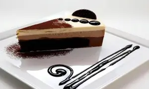 Deliciosa tarta de 3 chocolates, con capas de mousse y bizcocho, decorada con cacao y un toque de chocolate líquido.