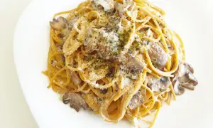 Espaguetis con nata y champiñones, cubiertos con queso rallado y hierbas aromáticas. Un plato cremoso y delicioso.