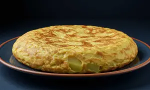 Tortilla de berenjena dorada y esponjosa, con trozos de patata visibles, servida en un plato azul.