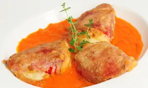 Pimientos rellenos de bacalao, dorados y crujientes, servidos en una cremosa salsa de pimientos rojos, adornados con tomillo fresco.