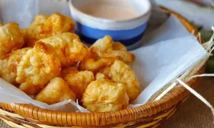 Cesta de mimbre con fritos de pixin dorados y crujientes, acompañados de una salsa rosada. ¡Un bocado delicioso!