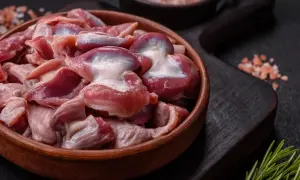 Un cuenco de madera lleno de mollejas de pollo crudas, listas para ser cocinadas. Sal rosada y romero al lado.