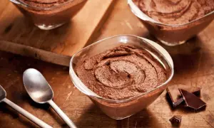 Delicioso mousse de chocolate en copas de cristal, listo para disfrutar. Trozos de chocolate negro al lado.