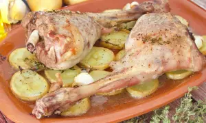 Dos jugosas piernas de cabrito al horno, tiernas y doradas, reposan sobre patatas asadas y dientes de ajo.