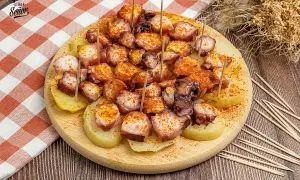 Pulpo a la gallega servido sobre patatas cocidas, espolvoreado con pimentón y servido con palillos.