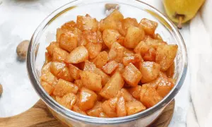 Trozos de manzana asada en freidora de aire, cubiertos de canela, en un bol de cristal.