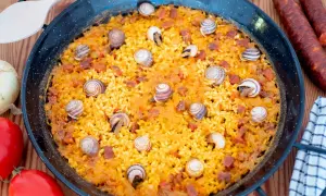 Arroz con caracoles en paellera, con trozos de chorizo y decorado con caracoles. Ingredientes frescos alrededor.