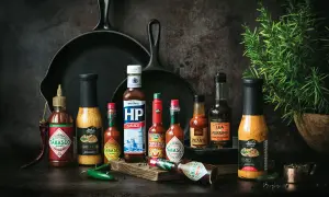 Variedad de salsas para carnes, incluyendo Tabasco, HP Sauce y Lea & Perrins, junto a chiles y romero.