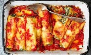 Canelones de atún horneados con salsa de tomate y espinacas, listos para servir en una bandeja.