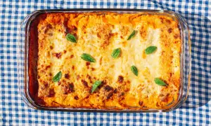Bandeja de canelones de espinacas gratinados, decorados con hojas de albahaca fresca, sobre un mantel de cuadros azules y blancos.