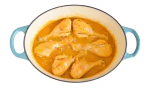 Pollo en salsa dorada, cocinándose en una olla azul. Las piezas de pollo están tiernas y cubiertas de una rica salsa.