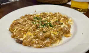 Delicioso revuelto de bacalao con trocitos de frutos secos y perejil picado, servido en plato blanco.