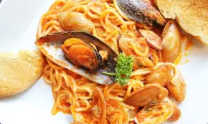 Espaguetis con almejas y mejillones en salsa roja, servidos con pan tostado. Un plato de pasta marinera delicioso.