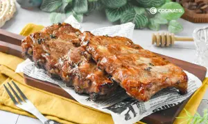 Costillas a la miel, jugosas y glaseadas, servidas sobre papel de periódico y tabla de madera.
