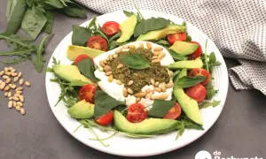 Deliciosa ensalada de burrata y pesto, con aguacate, tomates cherry y piñones.