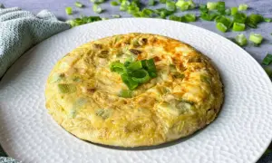 Tortilla de ajetes dorada y esponjosa, decorada con cebolleta fresca picada. Un plato sencillo y delicioso.