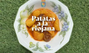 Un plato de patatas a la riojana, con trozos de chorizo y patata en una salsa rojiza, servido en una vajilla decorada con frutas y bayas.