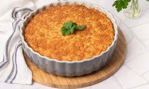 Pastel de bacalao dorado y crujiente, recién horneado en un molde gris, decorado con perejil fresco.
