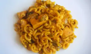 Fideuà de pollo con fideos rizados y trozos de pollo en salsa dorada, servida en plato blanco.