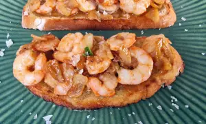 Tostadas con gambones al ajillo, cubiertas de ajo y perejil, espolvoreadas con sal marina gruesa sobre un plato verde.
