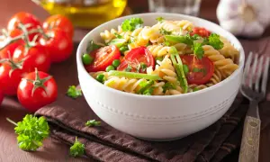 Un delicioso plato de pasta con verduras frescas, tomates cherry, guisantes y perejil.