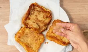 Torrijas de horchata doradas y crujientes, listas para disfrutar. Una mano espolvorea azúcar y canela sobre una de ellas.
